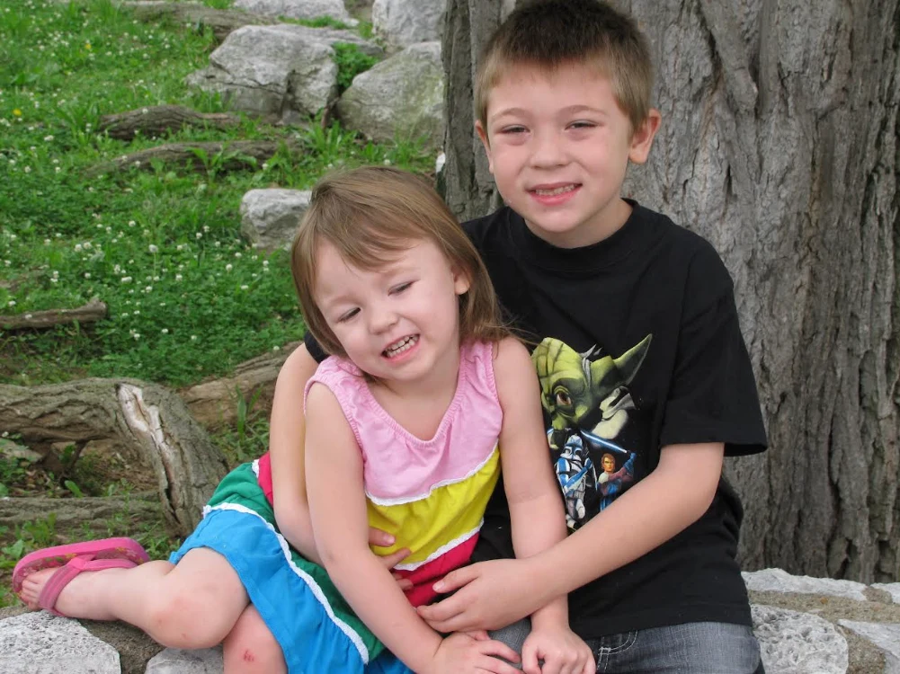 Shayne and his sister sitting together by a tree.